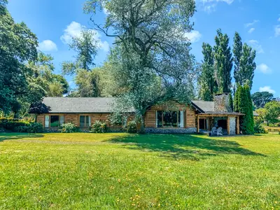 La casa de troncos entre álamos y árboles añosos, con el parque de césped al frente