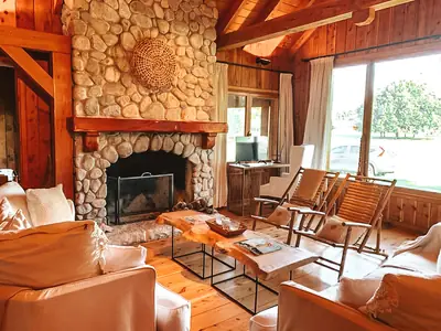 Living con hogar de piedra, sillones y ventanal al parque